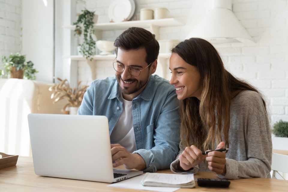 couple sitting at kitchen counter reviewing budget costs on laptop